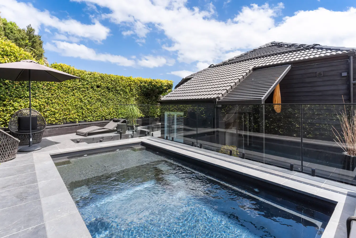 Frameless glass fencing around a dark-tiled pool with hedging