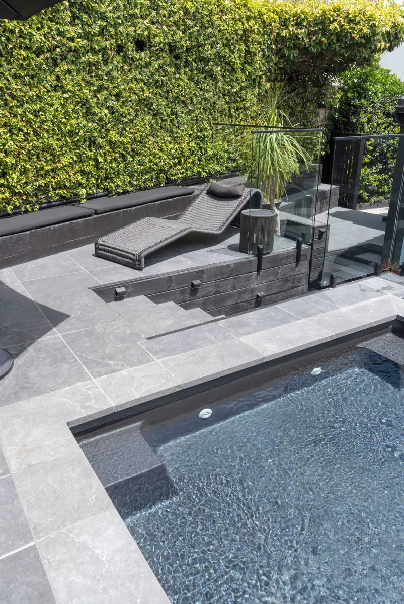 Sun lounger and dark tiled spa behind the glass pool barrier