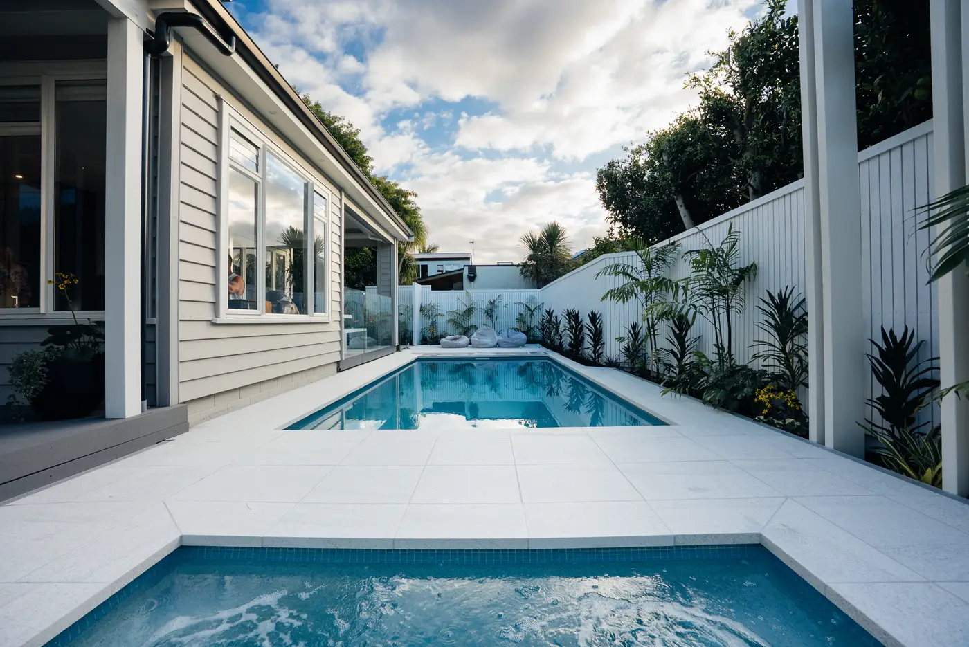 Pool and spa with white weatherboard house and aluminium screening